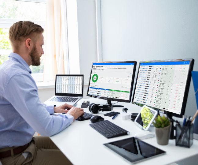 A man at his desk working on three computers simultaneously